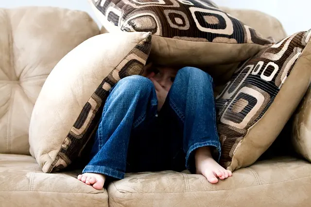 Enfant caché entre les coussins d'un canapé car il manque de confiance en lui.